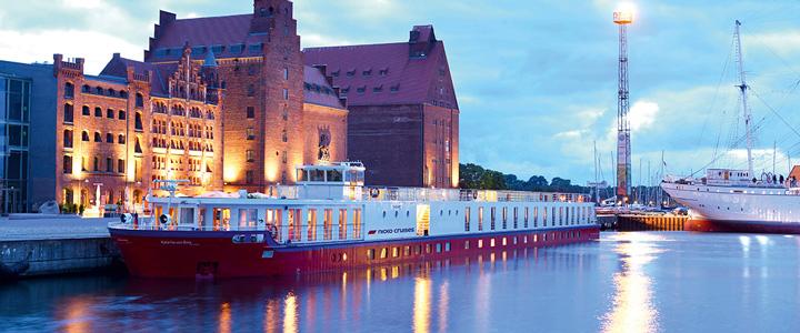 Die MS KATHARINA VON BORA liegt im Hafen am Kai. In der Abenddämmerung spiegeln sich Lichter im ruhigen Wasser.