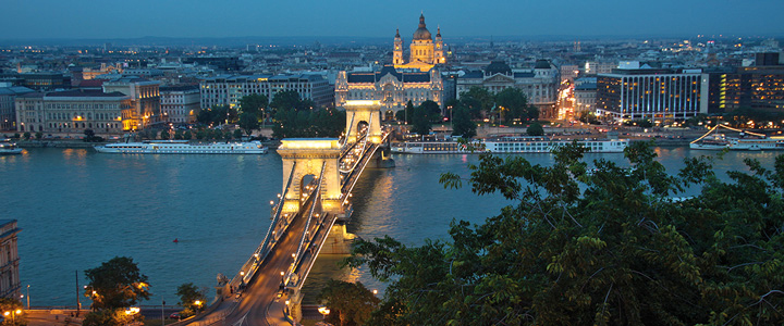 Die beleuchtete Kettenbrücke verbindet die Ufer von Budapest. Dahinter leuchtet die nächtliche Skyline der Stadt über der Donau.