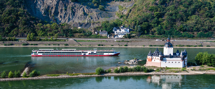 Die RHEIN SYMPHONIE gleitet über den Rhein, vorbei an historischen Uferbauten und Schlössern. Das Flussufer zeigt sich reich an alter Architektur.